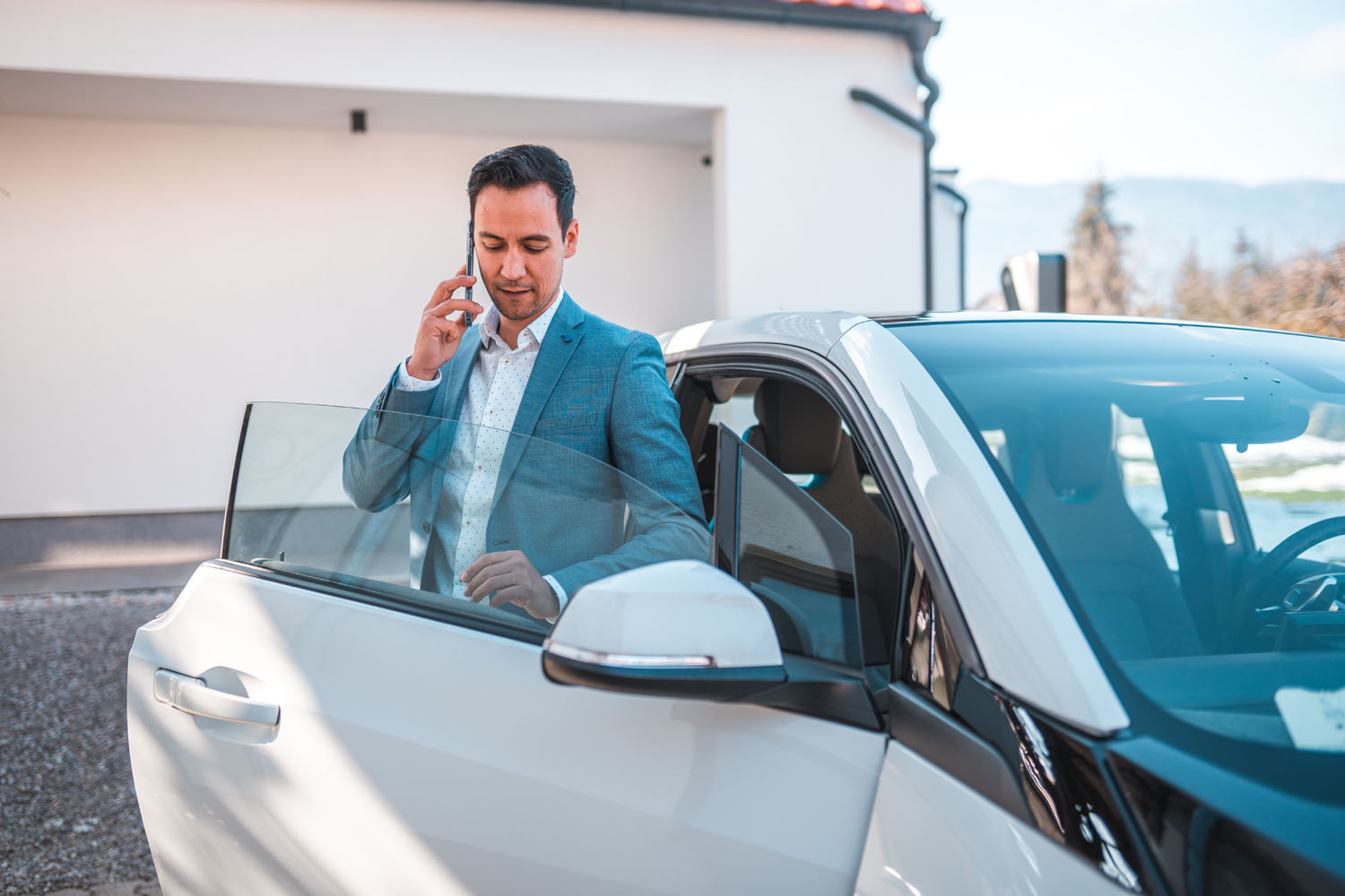 Confident Businessman Talking on Phone while close to his Electric Car