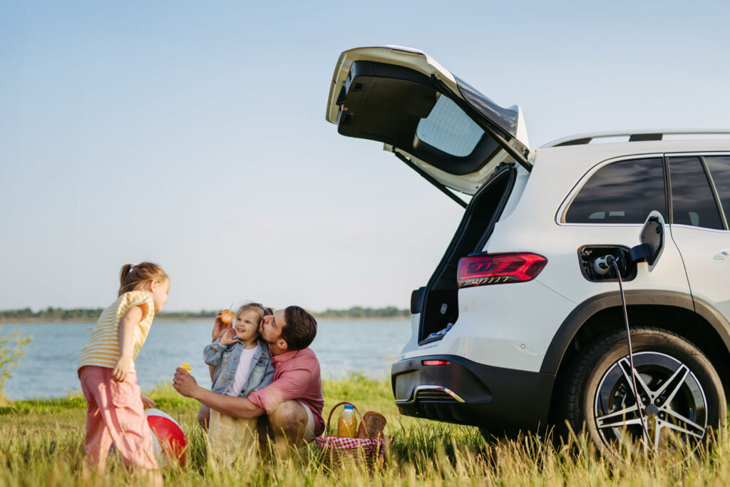 Happy family on the summer vacation having picnic, waiting for electric car to charge.